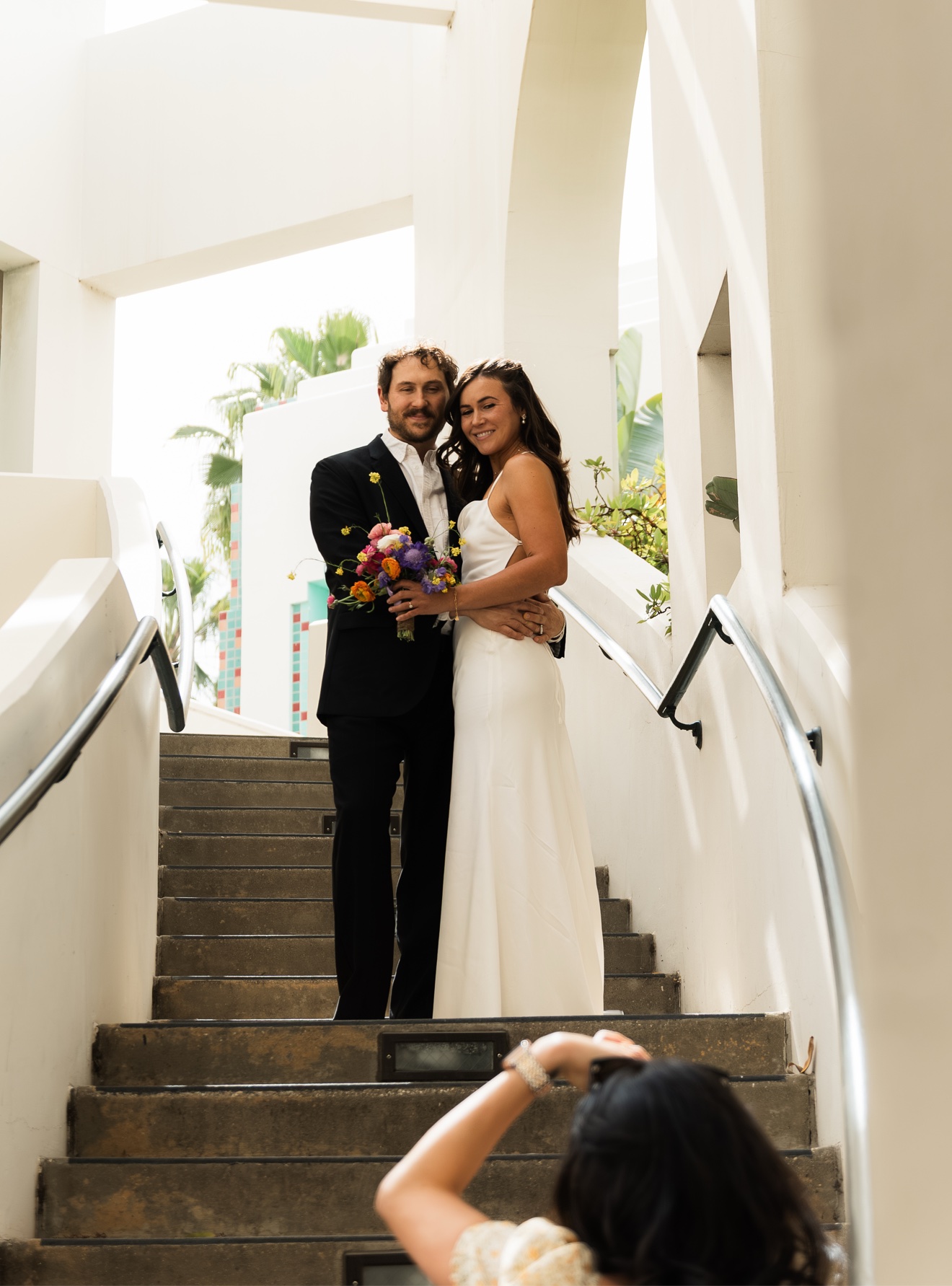 Photographer framing a wedding couple posed on a white staircase