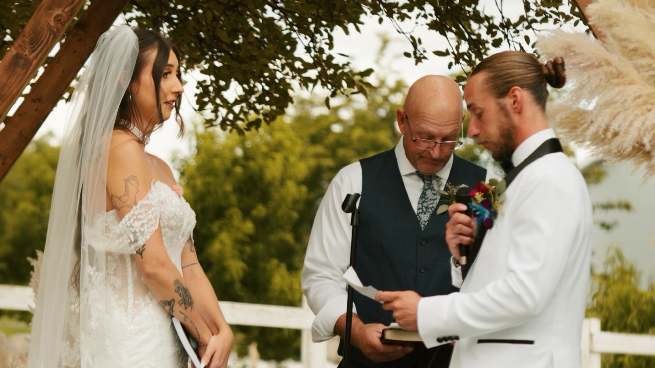 Bride and groom exchanging vows beneath a wooden arbor