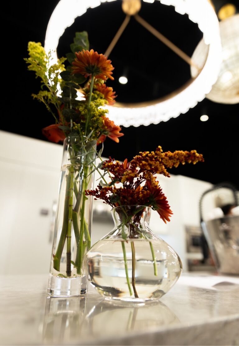 Glass bud vases with rust and orange flowers on a marble counter