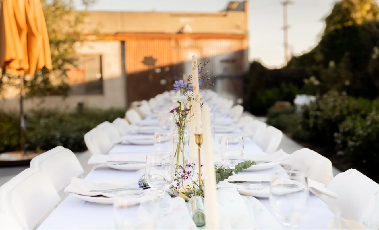 A long reception table at golden hour with taper candles and bud vases